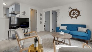 A modern living room with a flat-screen TV, a blue sofa, and a wooden coffee table. - Coastal Cottage STEPS to BEACH and downtown Old Orchard Beach - Prime Location (Old Orchard Beach)