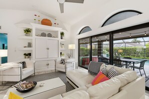 A modern living room with a white sofa, a coffee table, and a dining area with outdoor seating. - Beachside Bliss in Marco Island (Marco Island)