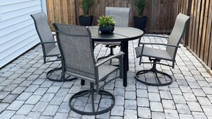 A patio with a round table and four chairs, surrounded by a wooden fence and potted plants.
