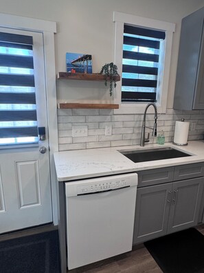 A kitchen with a built-in dishwasher, a sink, and a window with blinds.