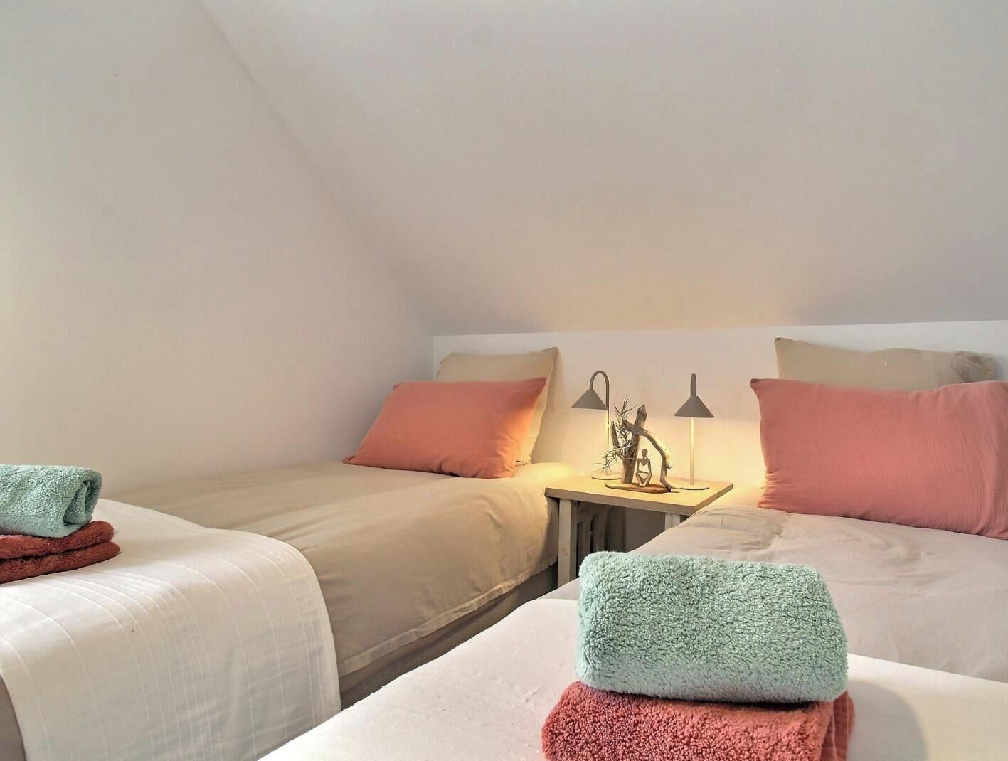 A bedroom with two beds, a nightstand with lamps, and a window.
