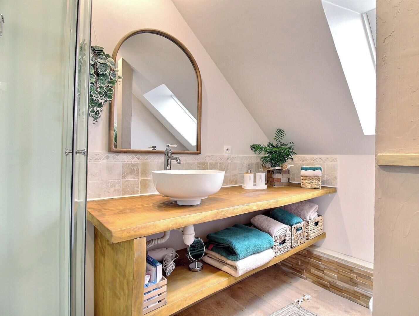 Ein Badezimmer mit weißem Waschbecken, Holzschrank, Spiegel, Handtuchhalter und einer kleinen Pflanze.