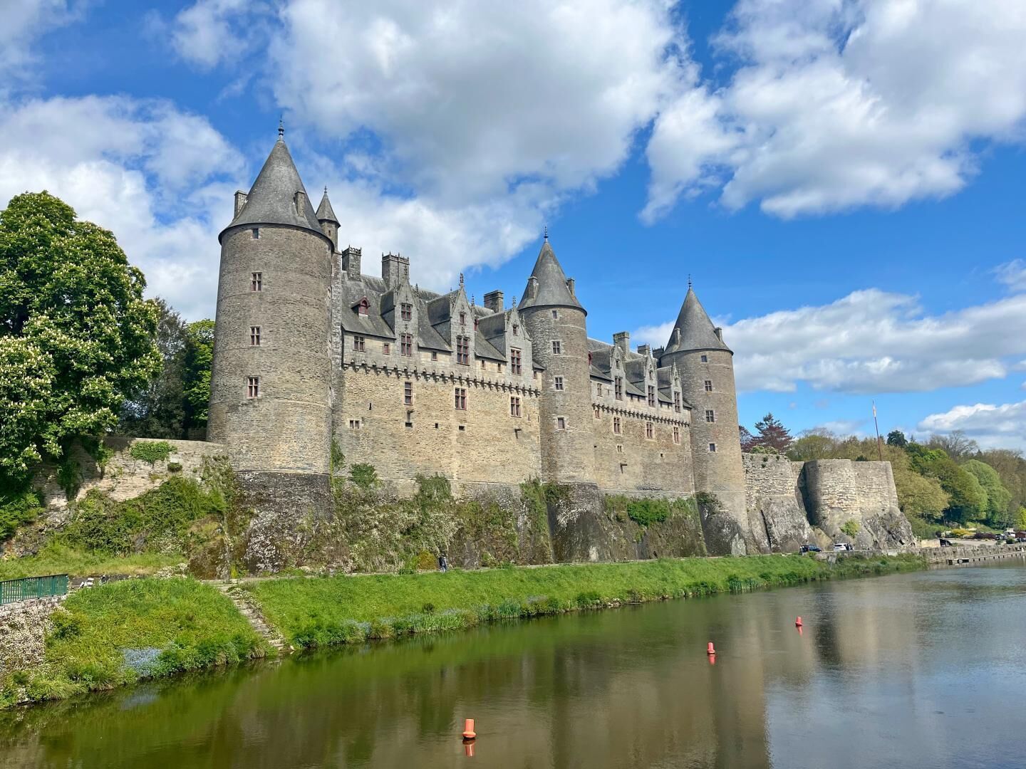 A historic stone castle with multiple towers, situated beside a calm river.
