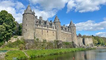 A historic stone castle with multiple towers, situated beside a calm river.