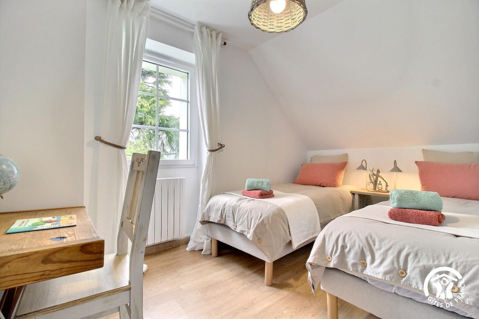 A bedroom with two beds, a wooden chair, a desk, a globe, and a window with curtains.