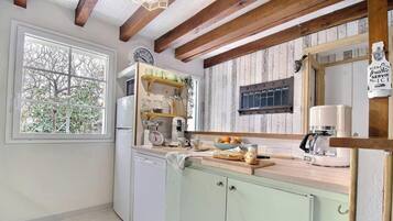 Una cocina con techo de madera, una ventana con vista a árboles, un reloj y una pizarra con la palabra 'Bienvenue'.