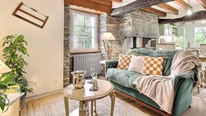 En hyggelig stue med en stenspis, træbjælker, en grøn sofa og et spiseområde.