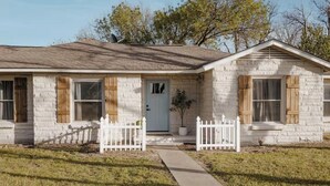 A two-story house with a stone facade, a front porch with a white picket fence, and a small garden. - Bagby Bunkhouse • Beautiful Cottage 7 minutes from Baylor and Magnolia • Pond (Waco)