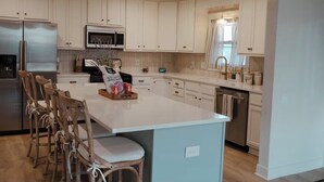 A modern kitchen with white cabinets, stainless steel appliances, and a central island with seating. - Bagby Bunkhouse • Beautiful Cottage 7 minutes from Baylor and Magnolia • Pond (Waco)