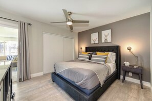 Une chambre à coucher avec un lit, un ventilateur de plafond, une table de chevet avec une lampe et une fenêtre avec des rideaux.