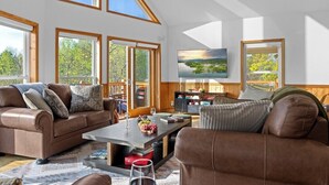 Ein geräumiges Wohnzimmer mit hoher Decke, großen Fenstern, einem Kamin und einem Fernseher.