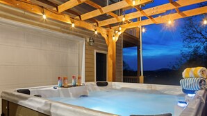 Ein Whirlpool unter einer Hollaube mit Lichterketten, einer Garagentür und Blick ins Freie im Abenddämmerung.
