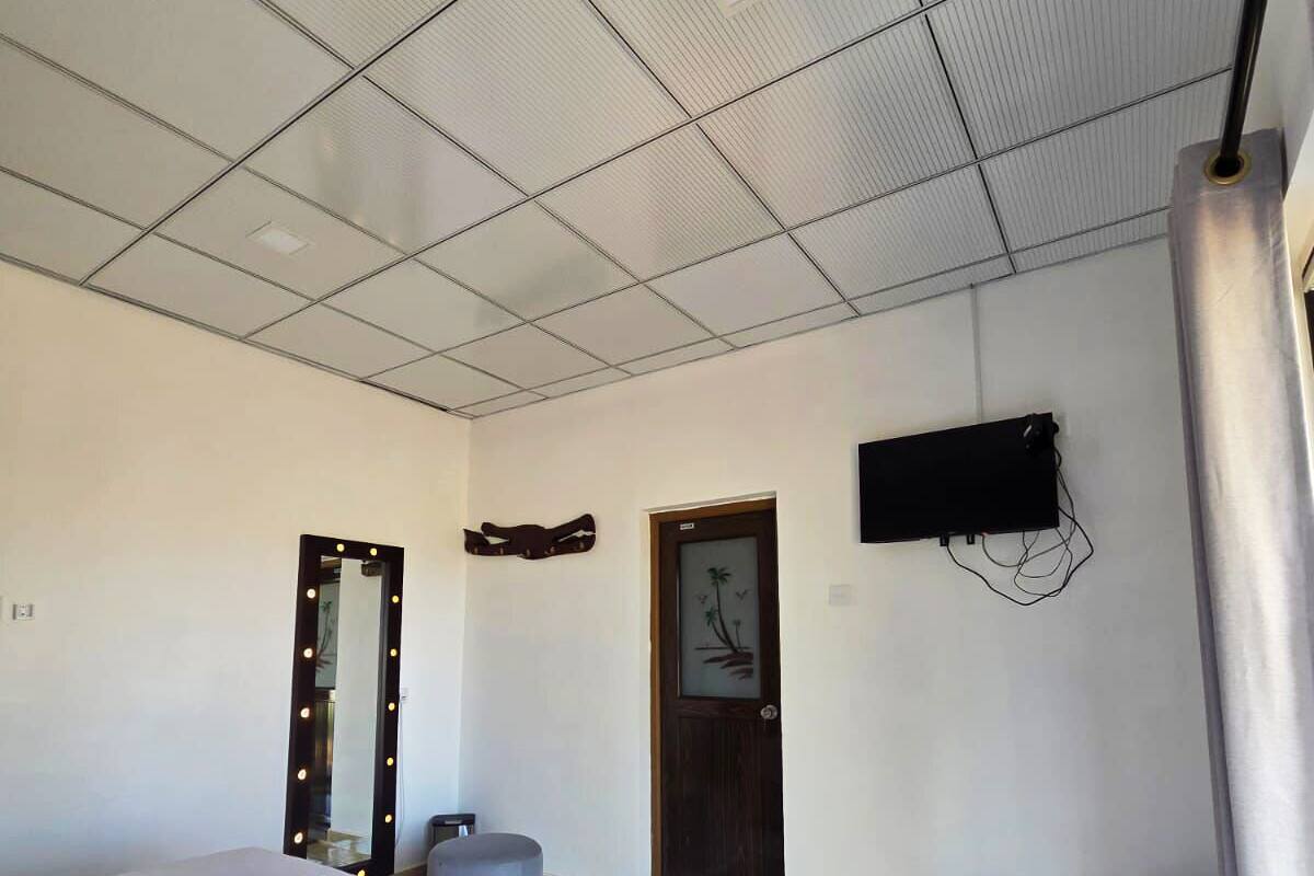 A hotel room with a bed, a mirror with lights, a television, a small table, and a door.