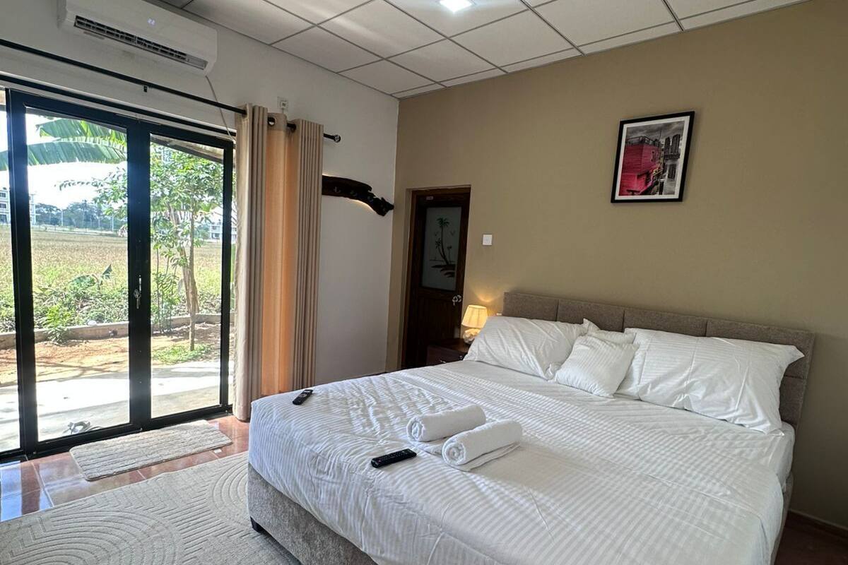 A hotel room with a large bed, a sliding glass door to the outside, a wall-mounted air conditioning unit, and a framed picture on the wall.