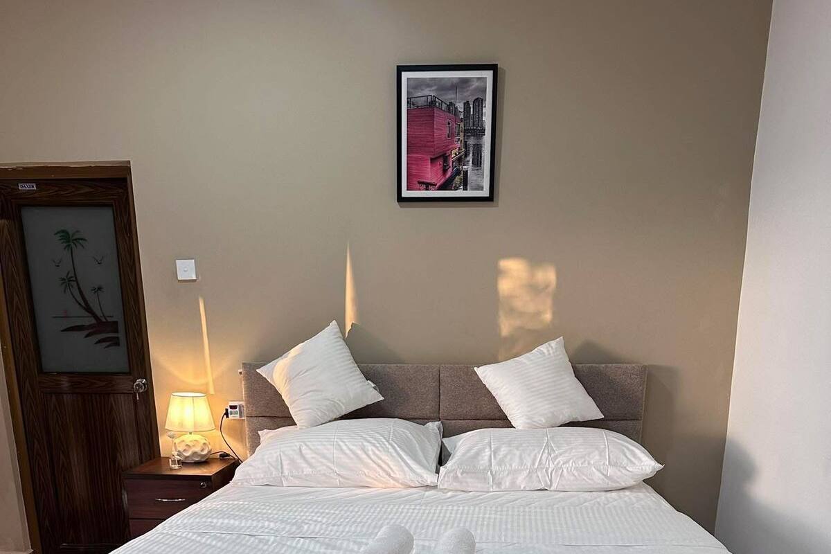 A neatly made bed with white linens and rolled towels, a bedside lamp, and a framed picture on the wall.