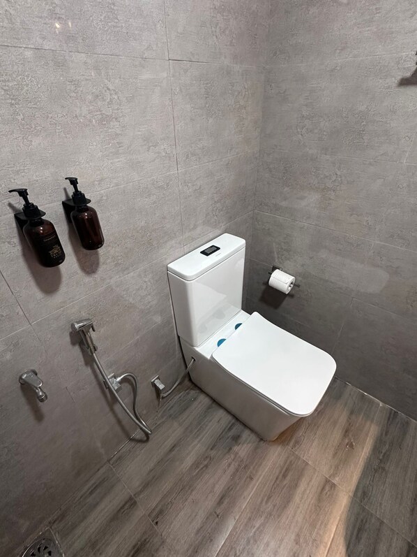 Un baño moderno con inodoro blanco, cabezal de ducha de mano y dos botellas de champú en la pared.