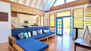 A spacious living area with a wooden ceiling, a blue sofa, and a view through the open door.