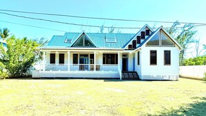 A two-story house with a blue roof, a porch with white railings, and a small attached structure with a white exterior.