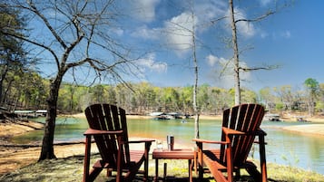 Due poltrone Adirondack, un tavolino e una vista limpida su un lago con barche sullo sfondo.