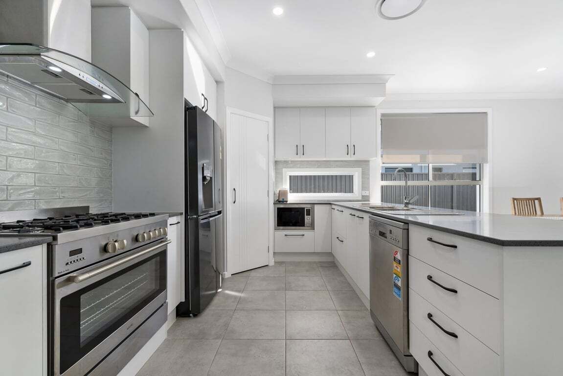 A modern kitchen with white cabinetry, stainless steel appliances, and a tiled floor.
