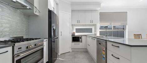 A modern kitchen with white cabinetry, stainless steel appliances, and a tiled floor.