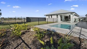 Une maison moderne avec une piscine, une cour clôturée et un ciel d’un bleu éclatant.