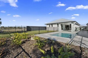 Ein modernes Haus mit Schwimmbad, umzäunter Garten und strahlend blauem Himmel.