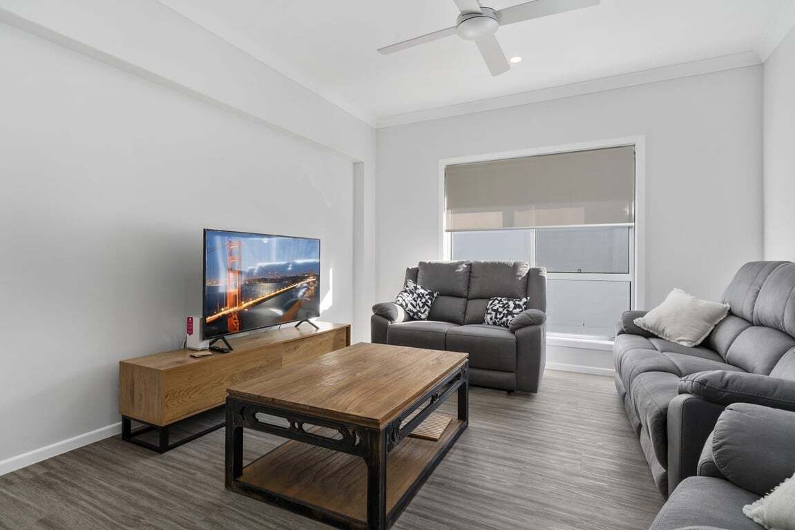 A modern living room with a flat-screen TV, a wooden coffee table, a grey sofa, and a ceiling fan.