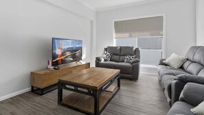 Un salon moderne avec un téléviseur à écran plat, une table basse en bois, un canapé gris et un ventilateur de plafond.