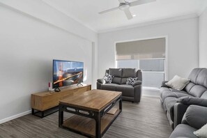 Ein modernes Wohnzimmer mit Flachbildfernseher, Couchtisch aus Holz, grauem Sofa und Deckenventilator.