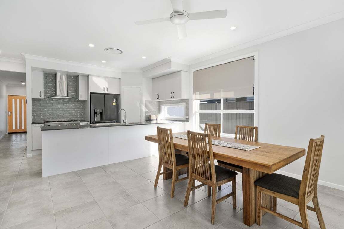 A modern kitchen with white cabinets, a central island, and a dining area with wooden chairs.