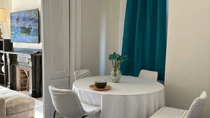 Un coin repas avec une table ronde, des chaises blanches, un vase de fleurs et des rideaux de couleur turquoise.