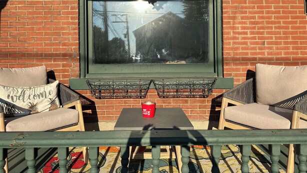 Une terrasse avec deux chaises, une petite table et une fenêtre donnant sur un immeuble et des arbres.