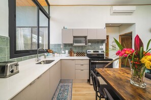 Eine kompakte Küche mit integriertem Mikrowellenherd, Herd und Spüle. Ein Essbereich mit Holztisch und Stühlen ist sichtbar.