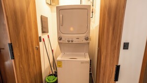 Eine kompakte, weiße Waschmaschine in einem schmalen Flur mit Holztüren und einem Wischtuch, das an der Wand lehnt.