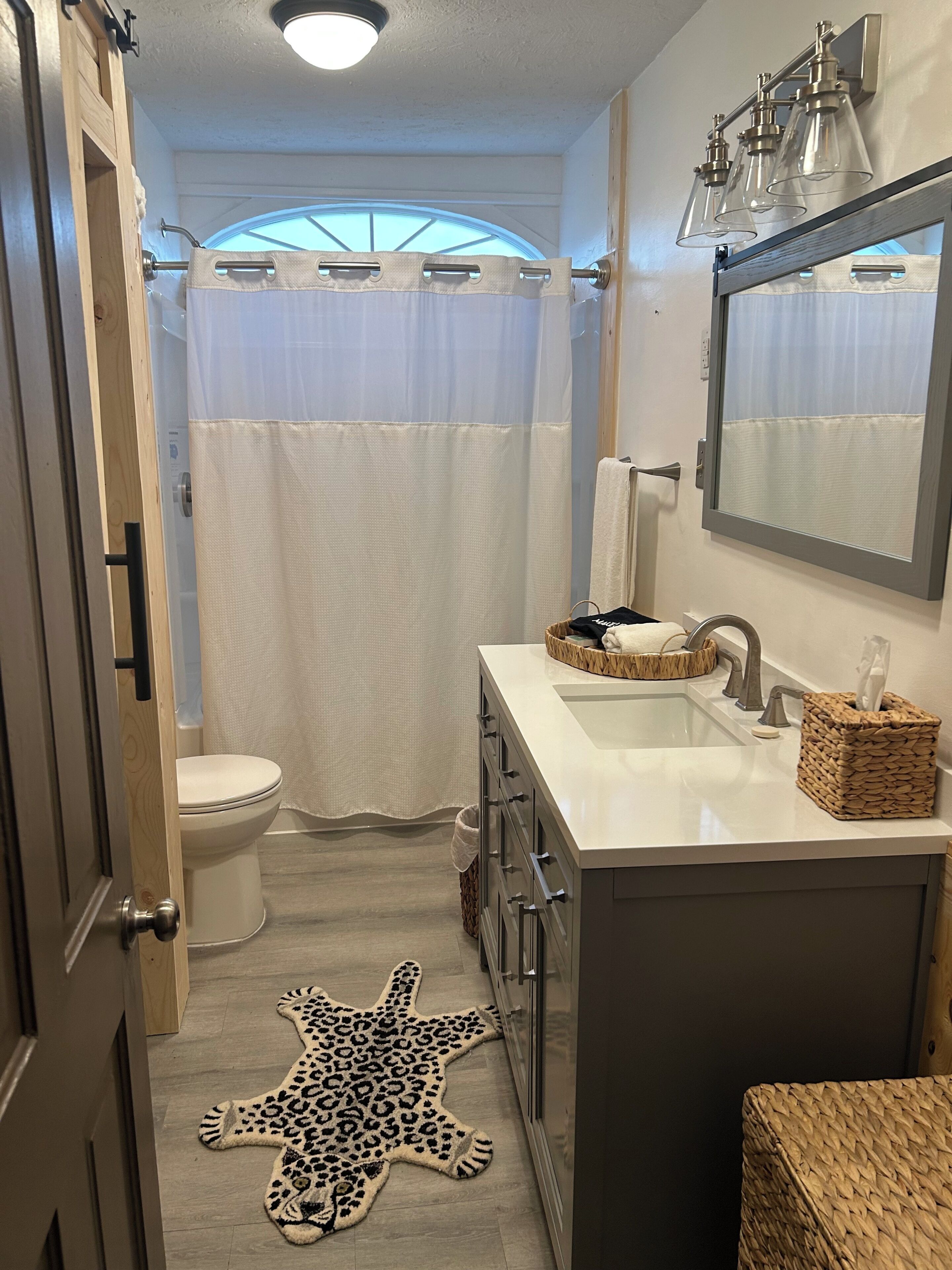 A bathroom with a toilet, a sink with a mirror, a star-patterned rug, and a shower curtain.