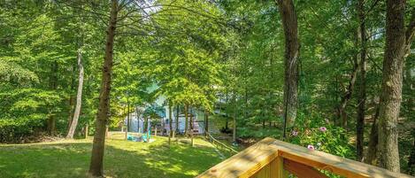 A wooden deck overlooking a lush green forest with a gazebo and outdoor seating area.