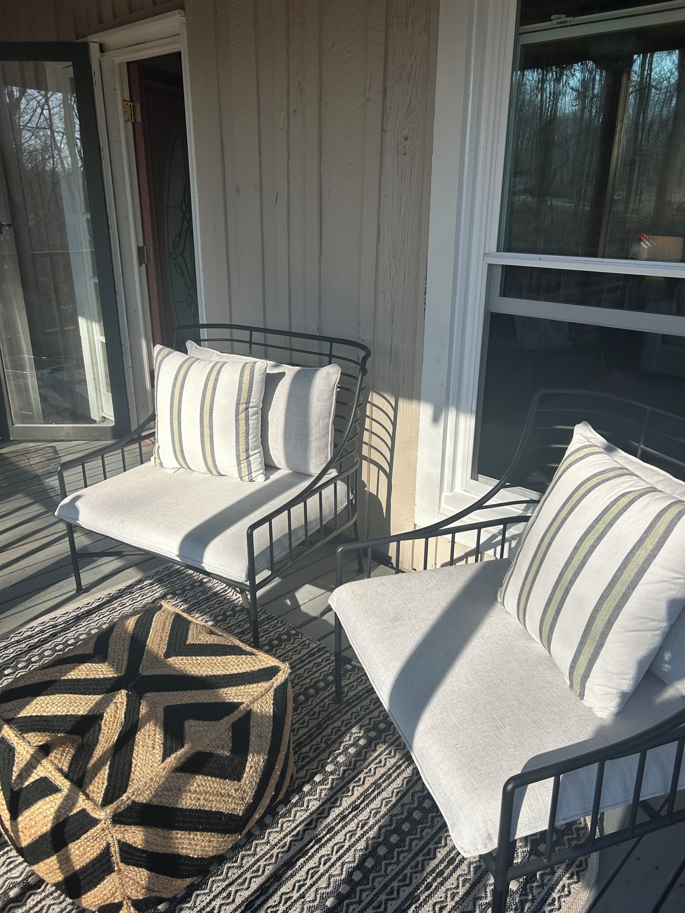 A covered porch with two metal-framed chairs, a woven rug, and a door leading to a screened area.