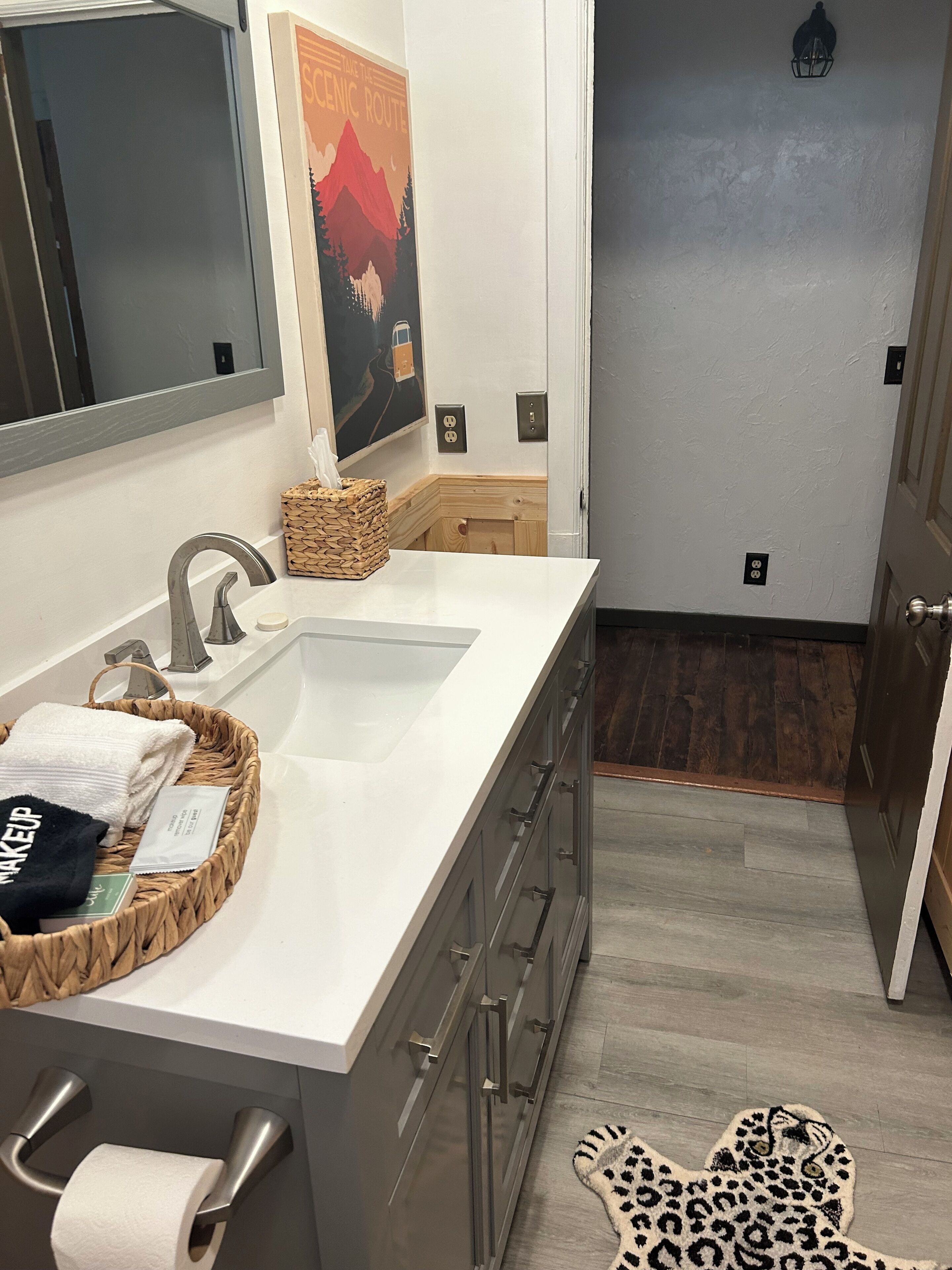 A bathroom with a white sink, a mirror, a towel, a basket, and a leopard print rug.