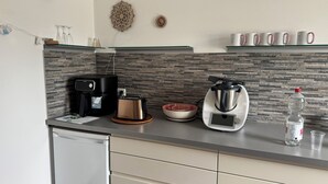 Une cuisine moderne équipée d’une machine à café, d’un grille-pain, d’un cuiseur à riz et d’une bouteille d’eau posée sur le plan de travail.