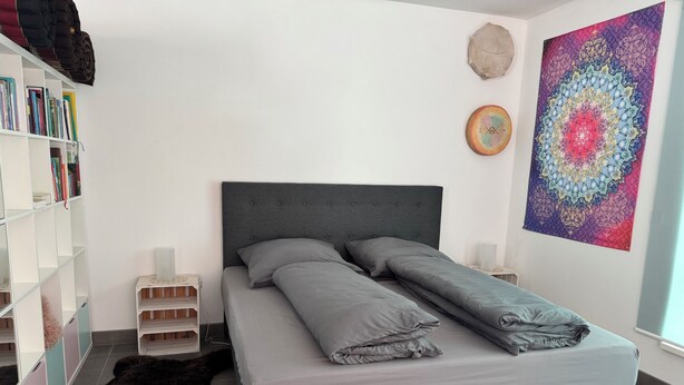 Une chambre à coucher bien rangée, avec un lit, des tables de chevet, une bibliothèque et une tapisserie aux couleurs vives.