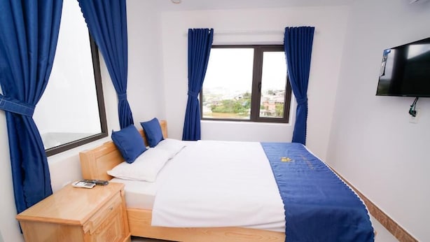 Un dormitorio con cama, mesita de noche de madera, televisor y cortinas.