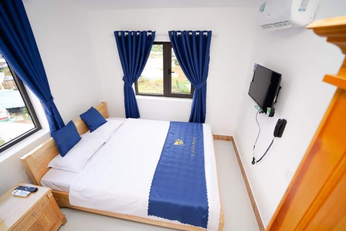 A bedroom with a bed, curtains, a TV, and a bedside table.