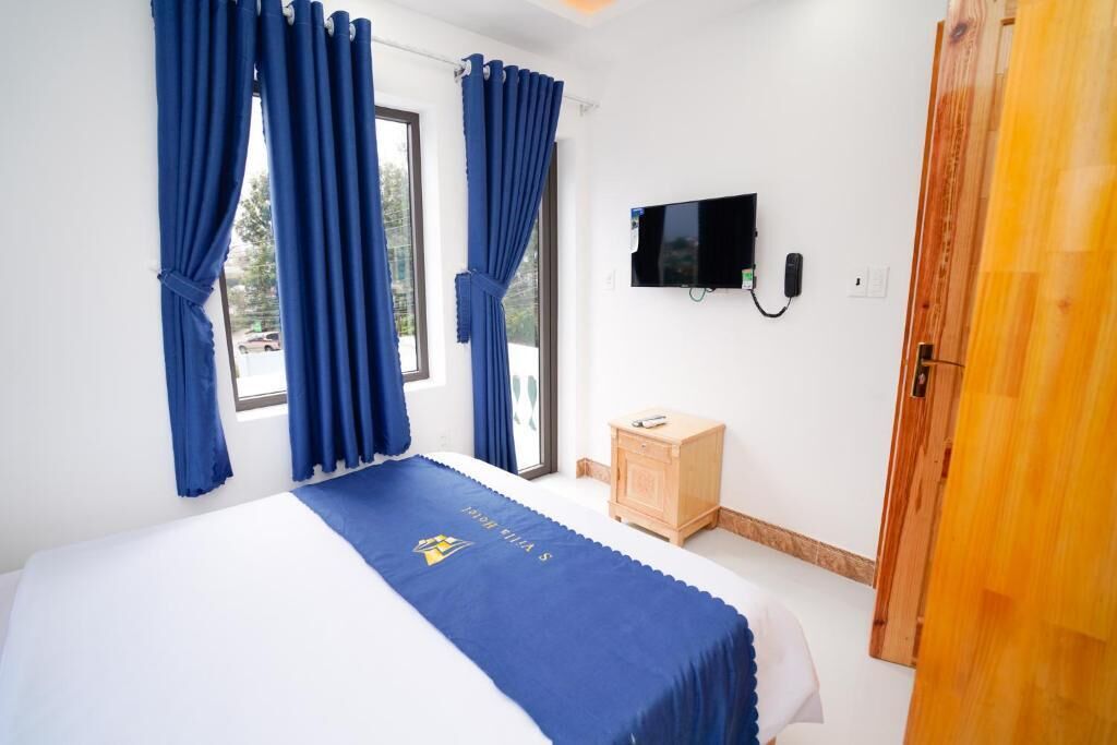 A hotel room with a bed, a TV, a wooden cabinet, and a door.