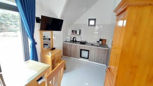Una cocina compacta equipada con microondas, tostadora y refrigerador pequeño. Hay una mesa de comedor de madera con sillas y un televisor montado en la pared.