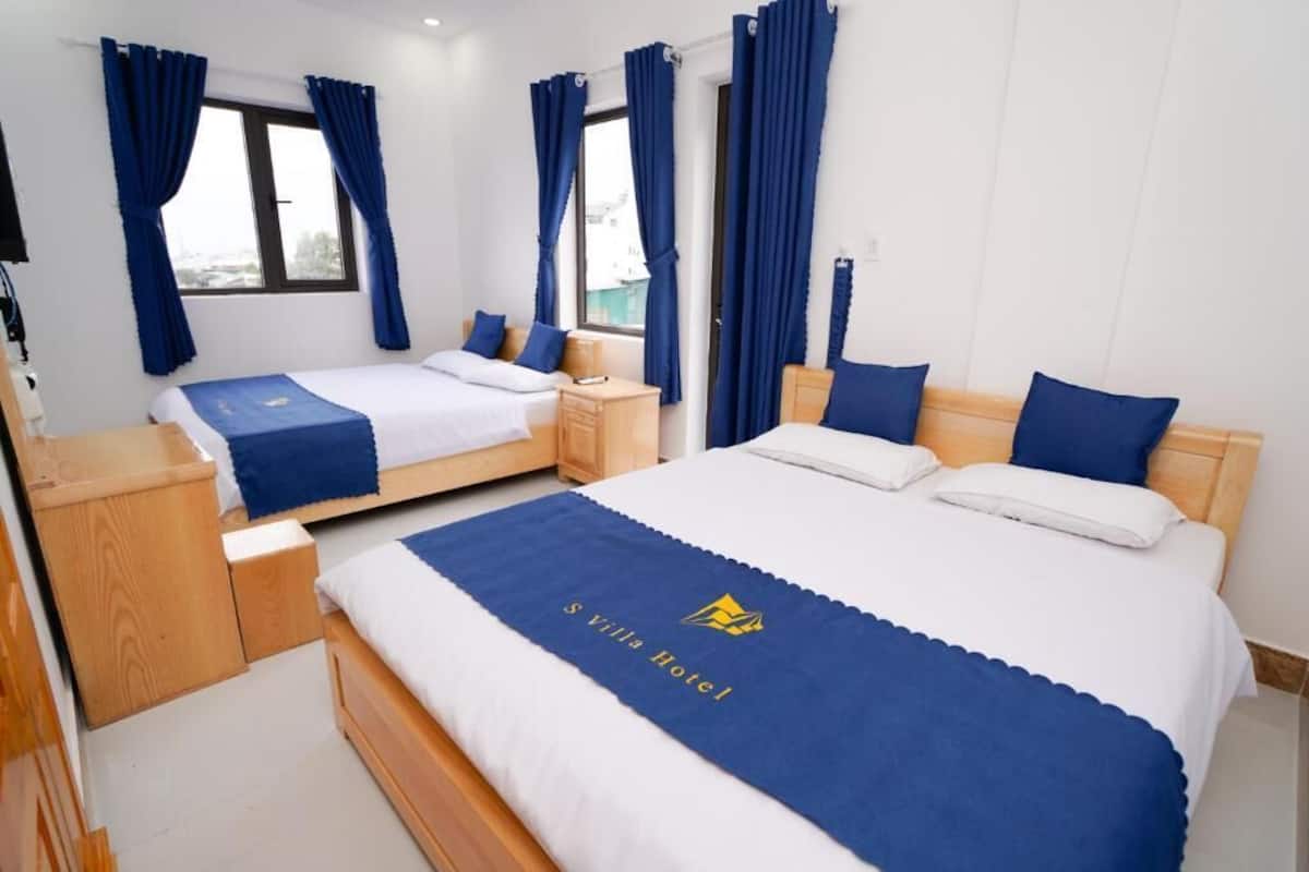 A hotel room with two beds, a wooden nightstand, a desk, and a window with curtains.