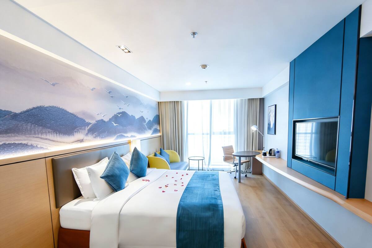 Una camera d'hotel con un letto, una scrivania, una televisione e un'ampia finestra.