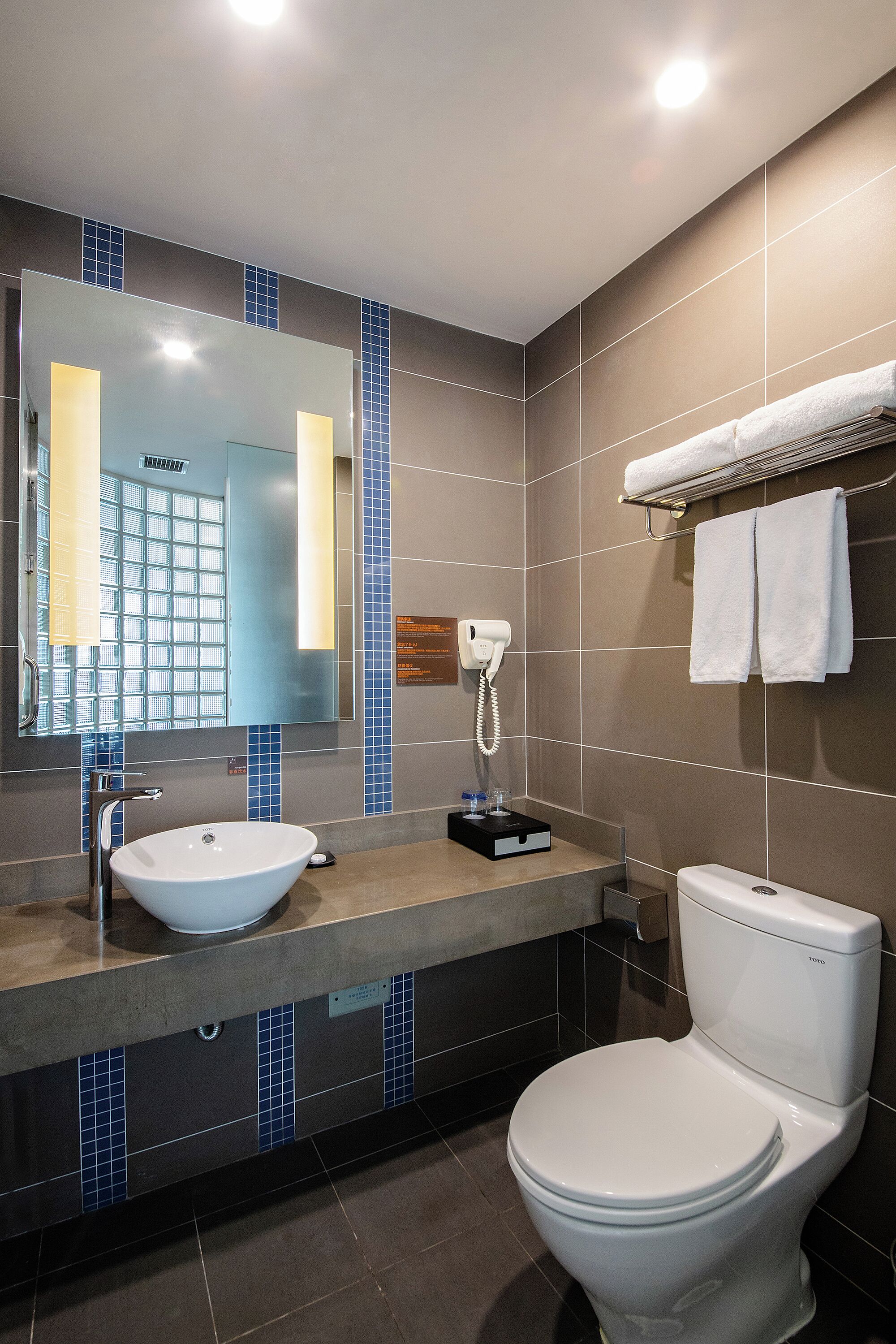 Ein modernes Badezimmer mit einem großen Spiegel, einem Waschbecken, einer Toilette und einem Handtuchhalter.