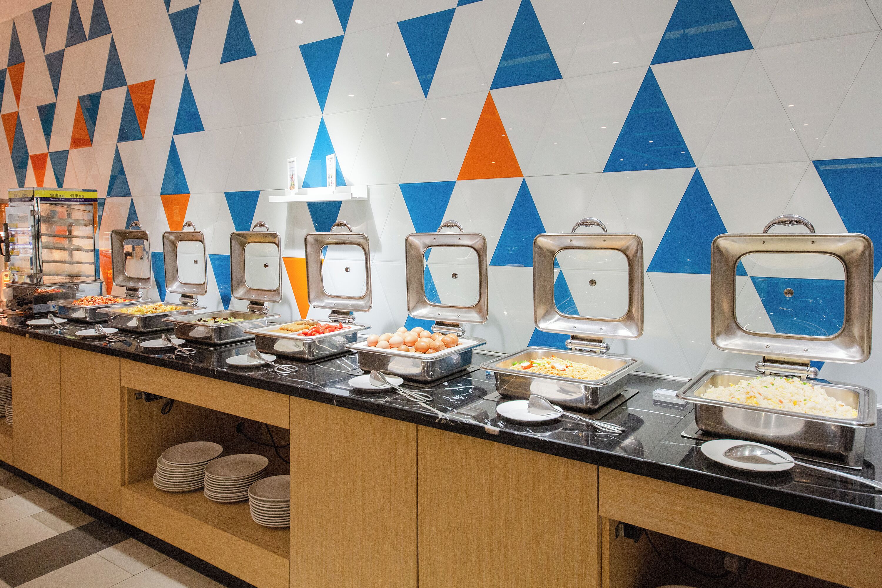 A buffet with various food items and a geometric patterned wall.
