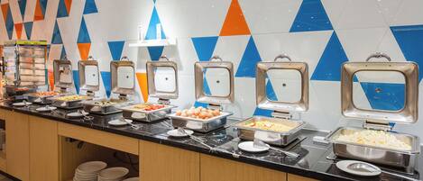 A buffet with various food items and a geometric patterned wall.